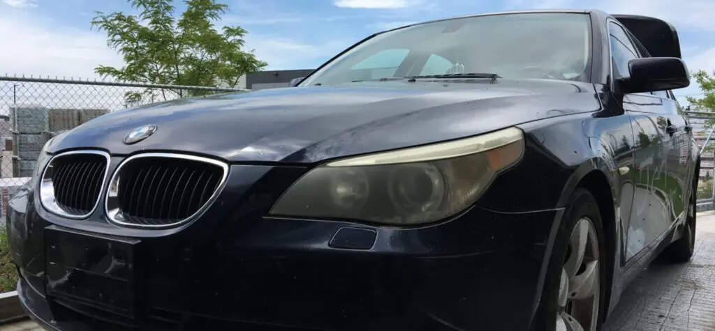 Black BMW sedan parked outdoors, showing signs of dirt and use on its exterior, ready for scrap car removal.