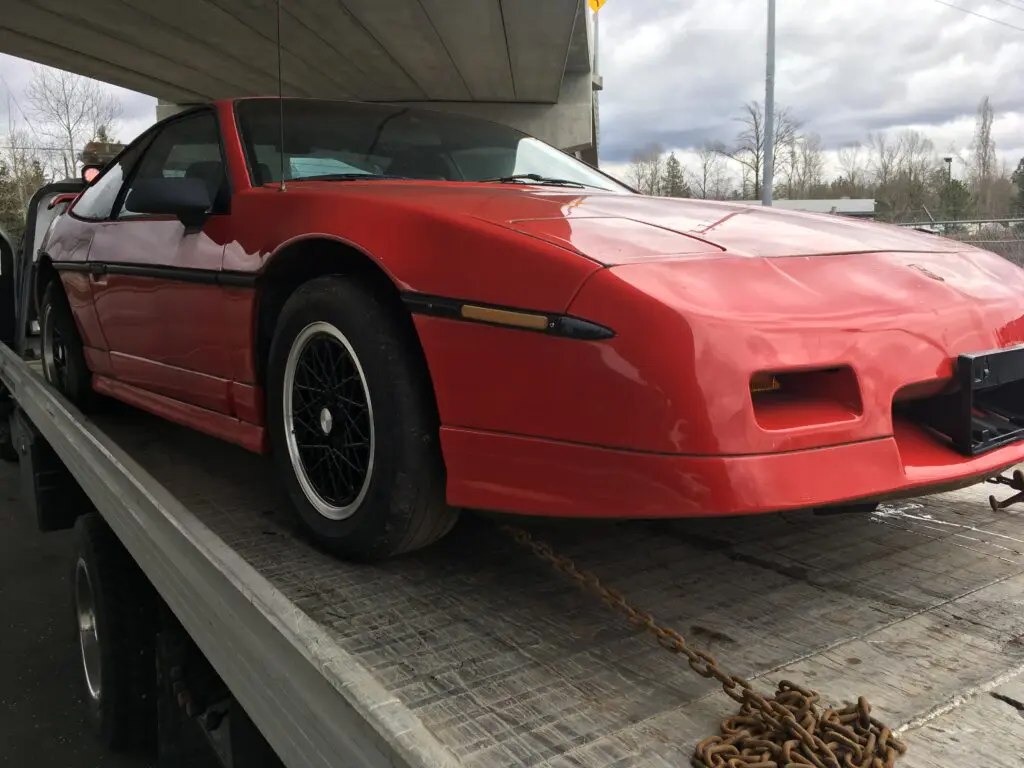 Red sports car being transported on a flatbed trailer for scrap car removal.