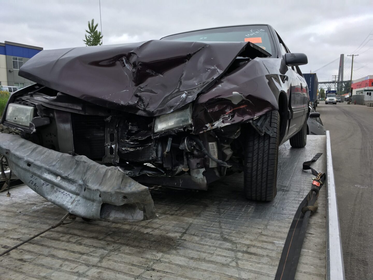 A damaged car with a crushed front end, awaiting scrap car removal, sitting on a tow truck.